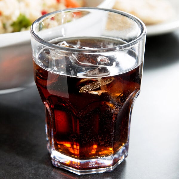 A Dinex clear plastic tumbler filled with brown liquid and ice next to a bowl of food.