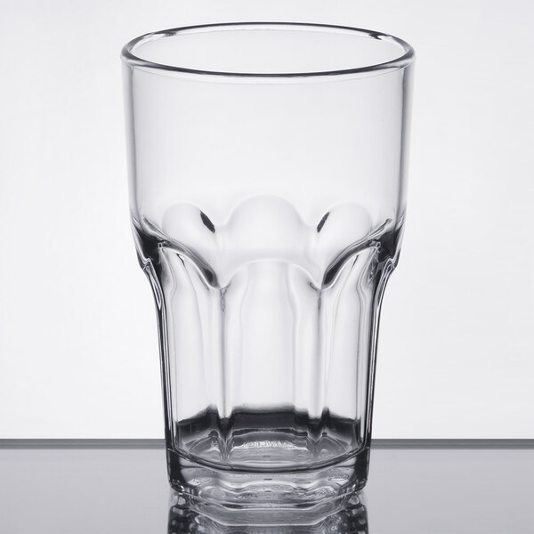 A close-up of a clear plastic Dinex tumbler with a rim on a table.