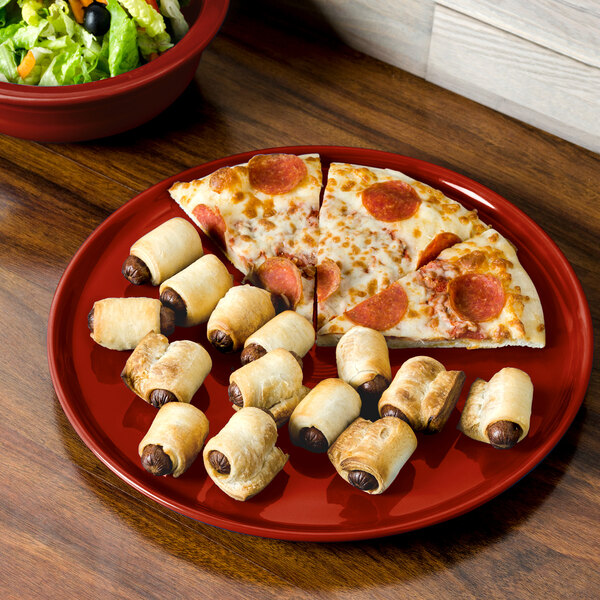 A Fiesta china plate with pizza and sausage rolls on a table.