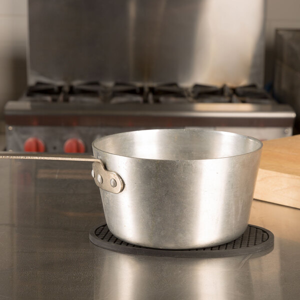 An oval black silicone trivet on a table with a metal pot on top.