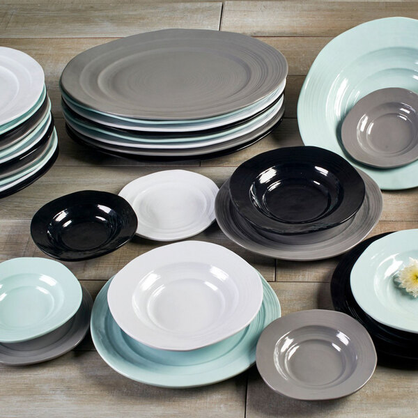 A group of black Elite Global Solutions Della Terra melamine plates on a wood surface.
