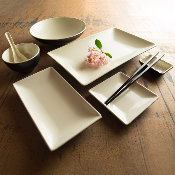 A white rectangular plate with a white bowl on a wood surface with a spoon inside.