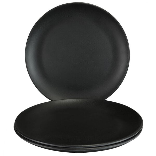 An Elite Global Solutions black melamine plate on a table with two more plates.