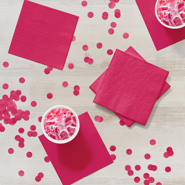 A group of cups of pink drinks and Creative Converting Hot Magenta Pink beverage napkins on a table.