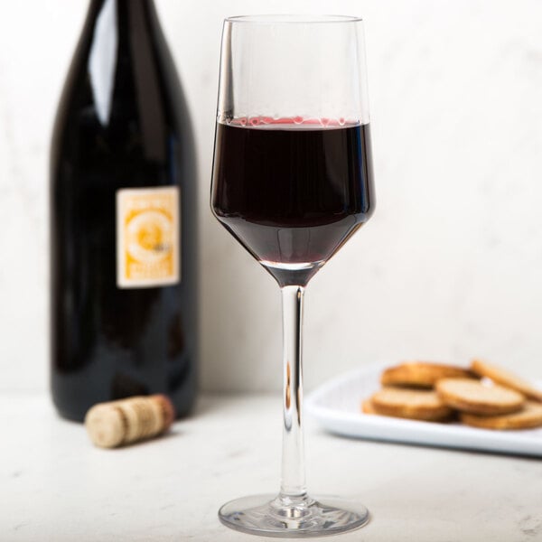 A close-up of a customizable Tritan plastic wine glass filled with wine next to a bottle of crackers.