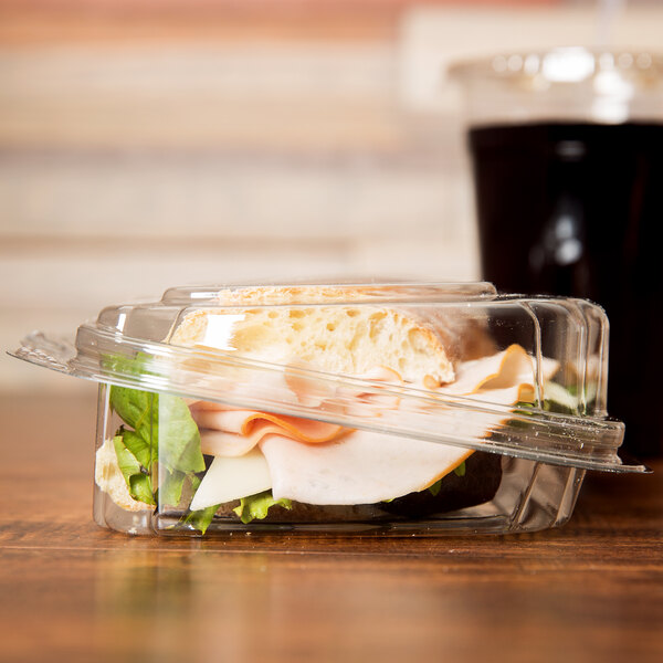 A sandwich and drink in a clear plastic container on a deli counter.