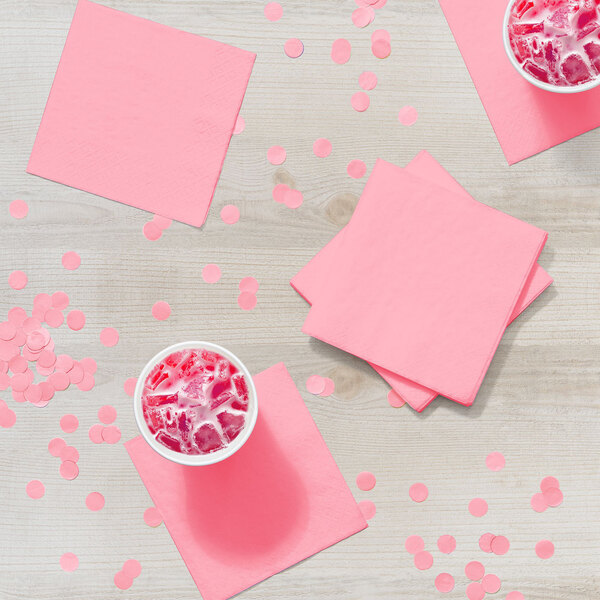 A stack of Classic Pink beverage napkins on a wooden table with pink drinks.