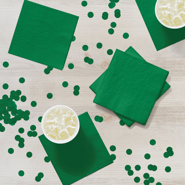 A table with emerald green Creative Converting beverage napkins and cups of liquid.