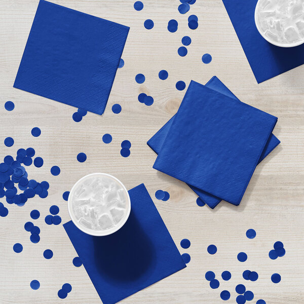 A blue Creative Converting beverage napkin on a table with blue cups of liquid.