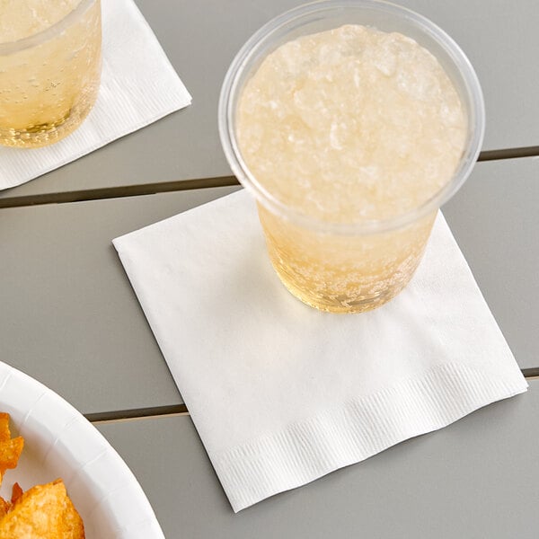 A pair of glasses of liquid on white Creative Converting beverage napkins with a plate of chips.