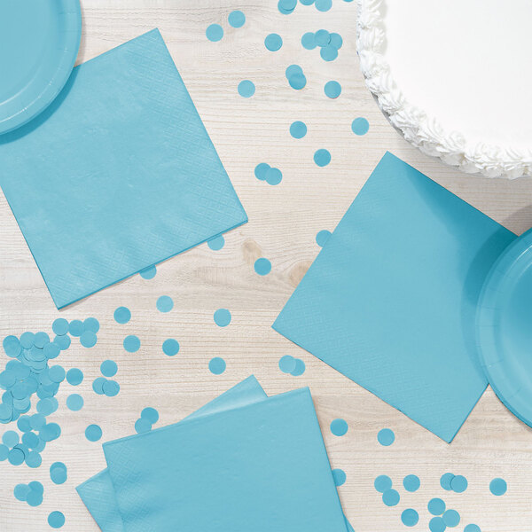 A table with blue paper napkins and confetti next to a blue plate.