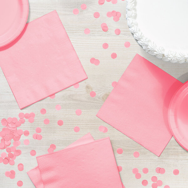 A pink napkin and paper plates on a table with confetti.