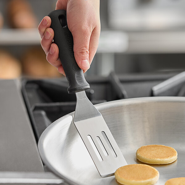 A hand holding a Tablecraft FirmGrip slotted mini turner over small pancakes.
