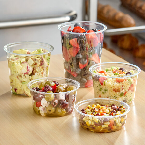 A set of clear round plastic deli containers filled with various salads and fruits.