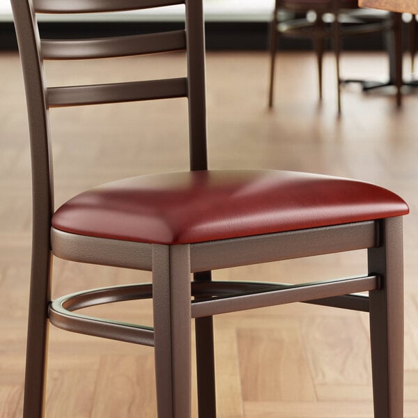 A Lancaster Table & Seating Spartan Series burgundy vinyl padded chair seat on a chair at a table in a restaurant.