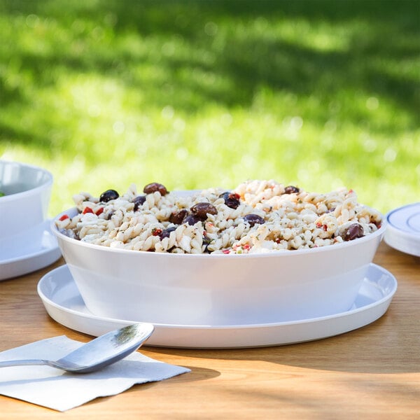 A white melamine bowl filled with pasta on a table with two white plates.