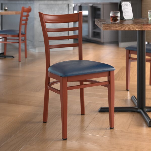 A Lancaster Table & Seating metal ladder back chair with mahogany wood grain finish and navy vinyl seat at a table in a restaurant.