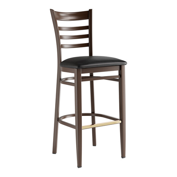 A Lancaster Table & Seating Spartan Series metal ladder back bar stool with dark walnut wood grain finish and black vinyl seat.