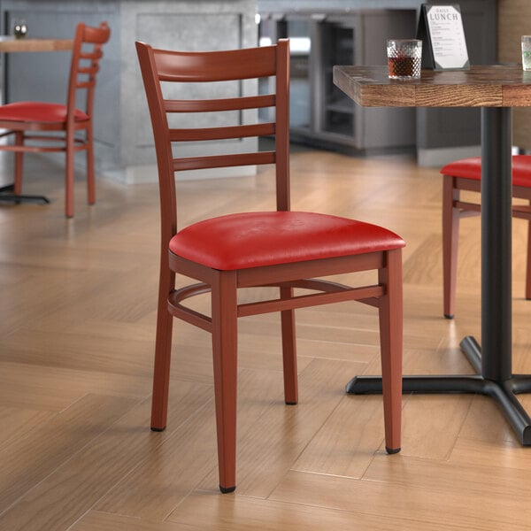 A Lancaster Table & Seating Spartan Series metal ladder back chair with mahogany wood grain finish and red vinyl seat at a table in a restaurant