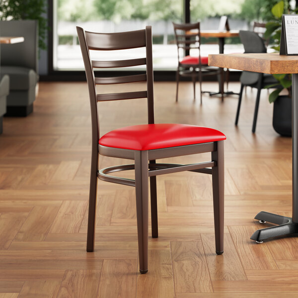 A Lancaster Table & Seating metal ladder back chair with dark walnut wood grain finish and red vinyl seat.