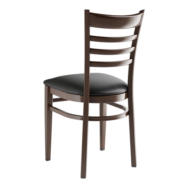 A Lancaster Table & Seating metal ladder back chair with dark walnut wood grain finish and black vinyl seat.