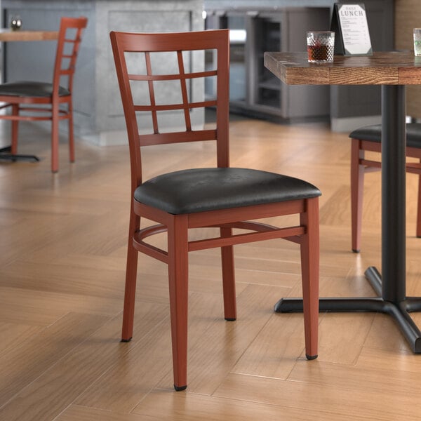 A Lancaster Table & Seating metal chair with mahogany wood grain finish and black vinyl seat at a table in a restaurant.