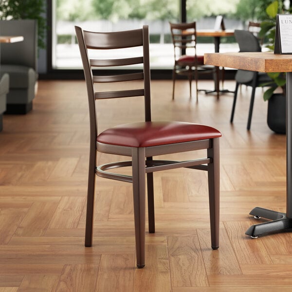 A Lancaster Table & Seating metal ladder back chair with dark walnut wood grain finish and burgundy vinyl seat at a restaurant table.