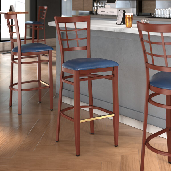 A Lancaster Table & Seating Spartan Series bar stool with navy blue vinyl seat and mahogany wood grain finish.