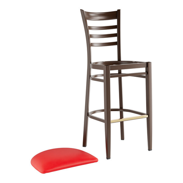 A metal ladder back bar stool with a dark walnut wood grain finish and a separate red vinyl seat cushion.