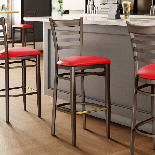 A metal bar stool with a dark walnut wood grain finish, ladder back design, and a red vinyl seat.