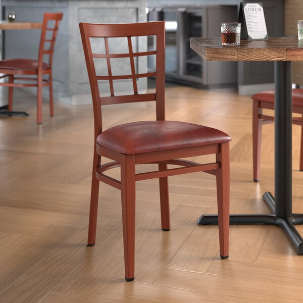 A Lancaster Table & Seating metal chair with mahogany wood grain finish and burgundy vinyl seat at a table in a restaurant.