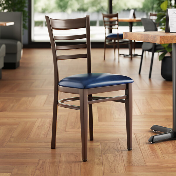 A Lancaster Table & Seating metal ladder back chair with dark walnut wood grain finish and navy vinyl seat in a restaurant.