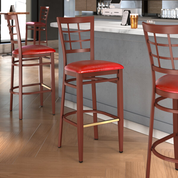 A Lancaster Table & Seating red metal bar stool with mahogany wood grain finish and red vinyl seat.