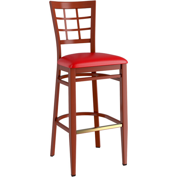 A Lancaster Table & Seating red metal bar stool with mahogany wood grain finish and red vinyl seat.