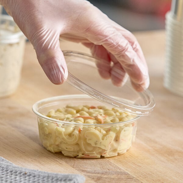 A clear 8 oz. round plastic deli container with a lid being placed on top, filled with macaroni salad.