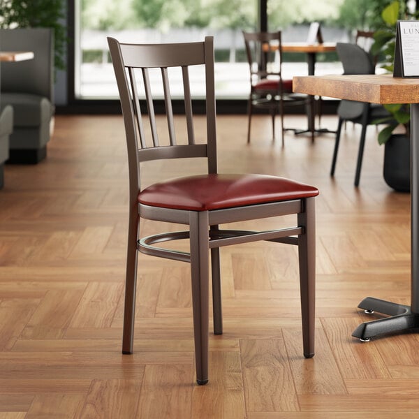 A Lancaster Table & Seating metal slat back chair with dark walnut wood grain finish and burgundy vinyl seat.