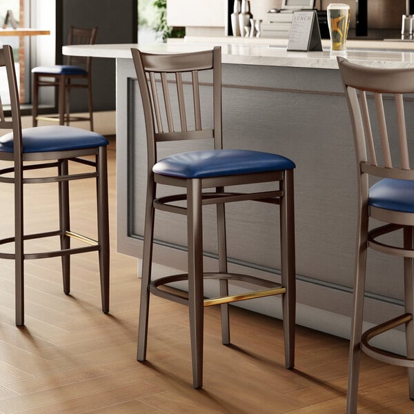 A group of three Lancaster Table & Seating metal slat back bar stools with navy vinyl seats.