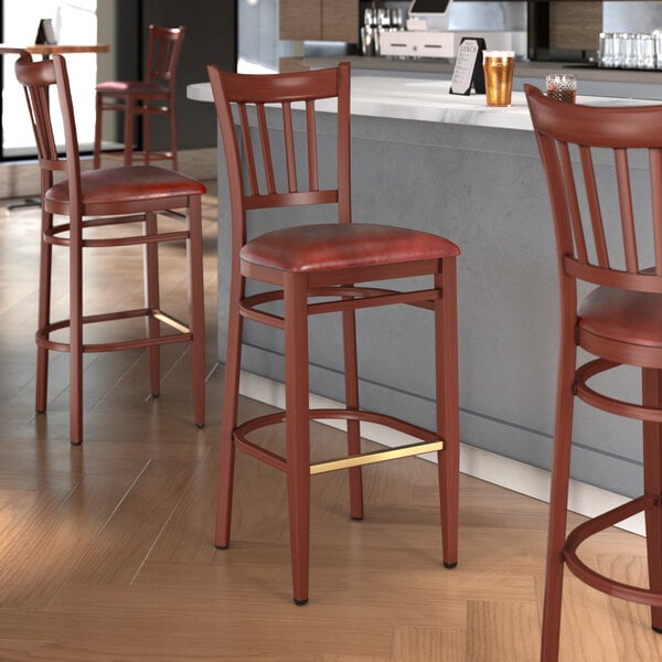 A group of Lancaster Table & Seating metal slat back bar stools with mahogany wood grain finish and burgundy vinyl seats.