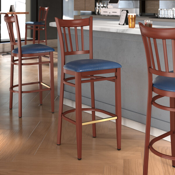 A Lancaster Table & Seating Spartan Series bar stool with navy vinyl seat and mahogany wood grain finish.