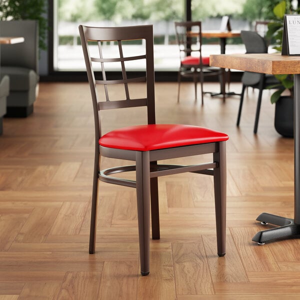 A Lancaster Table & Seating Spartan Series metal window back chair with dark walnut wood grain finish and red vinyl seat.