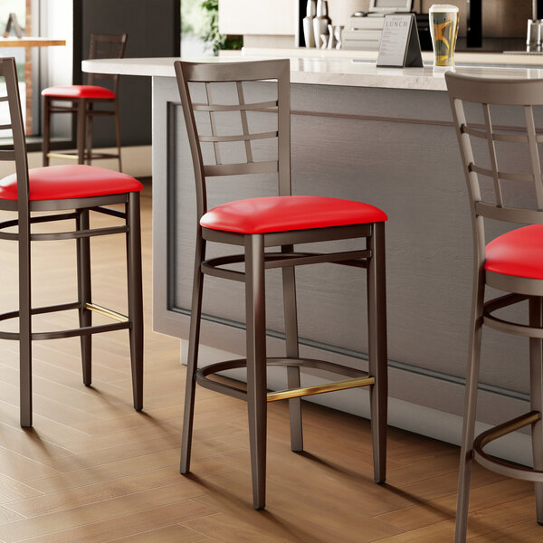 A group of three Lancaster Table & Seating red bar stools with black metal legs and dark walnut wood grain accents.