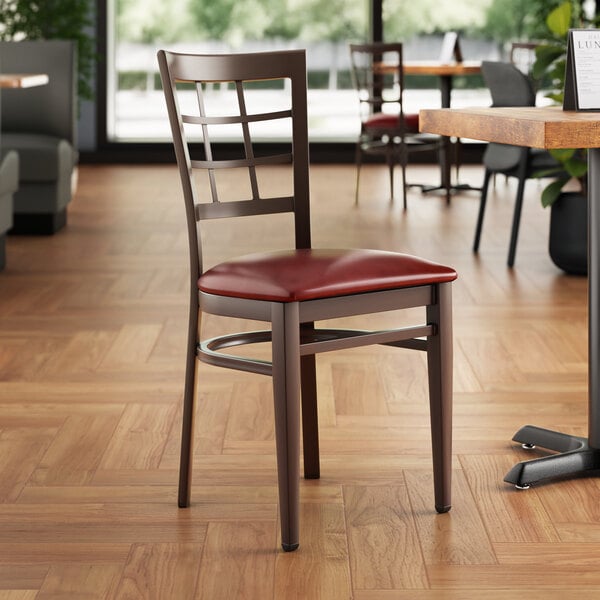 A Lancaster Table & Seating metal window back chair with dark walnut wood grain finish and a burgundy vinyl seat.