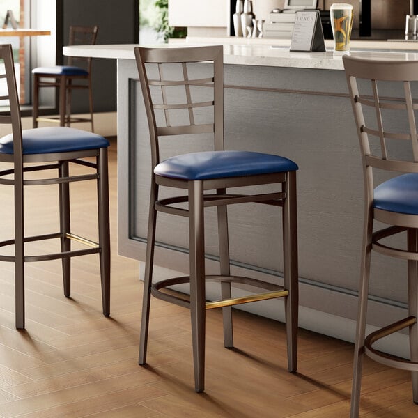 A Lancaster Table & Seating bar stool with a blue seat and metal legs.