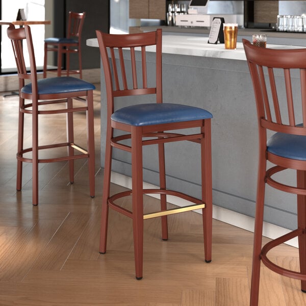 A Lancaster Table & Seating metal slat back bar stool with mahogany wood grain finish and navy vinyl seat.