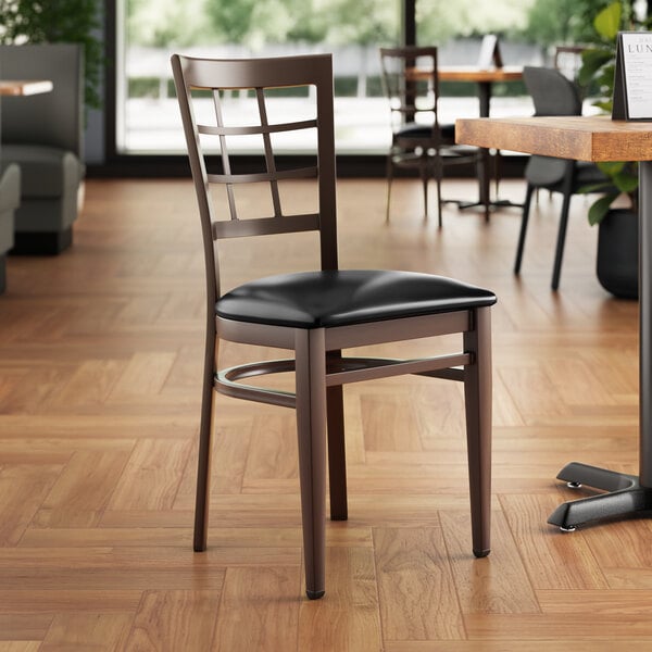 A Lancaster Table & Seating metal chair with dark walnut wood grain finish and black vinyl seat.