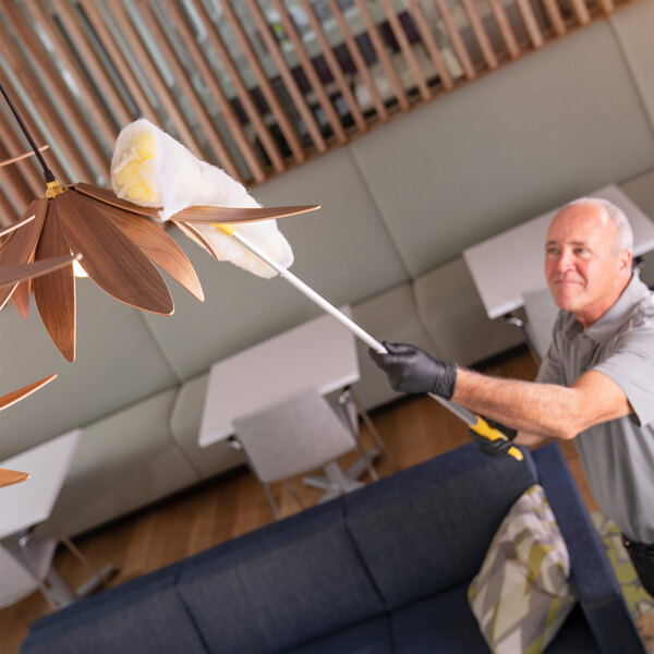 A person using a 3M Easy Trap duster sheet attached to an extension pole to clean a ceiling light fixture.