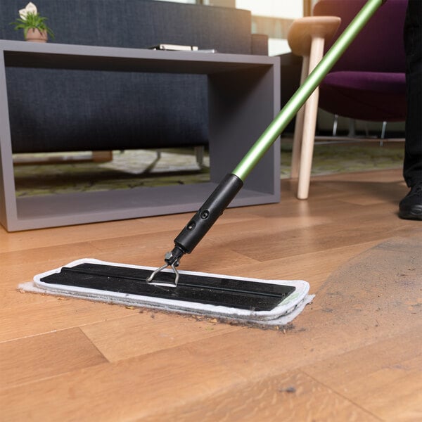 A flat mop with a green handle using a 3M Easy Trap duster sheet to clean dust and debris from a hardwood floor.