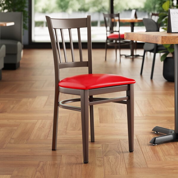 A Lancaster Table & Seating Spartan Series metal slat back chair with dark walnut wood grain finish and red vinyl seat.