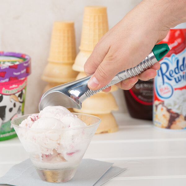 A hand using a Vollrath aluminum ice cream scoop to serve green ice cream into a bowl.