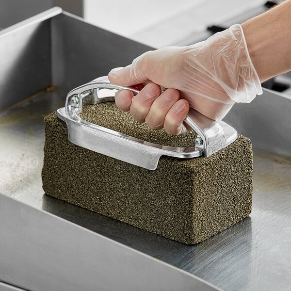 A hand wearing a plastic glove holding a Grill-Brick grill cleaner.